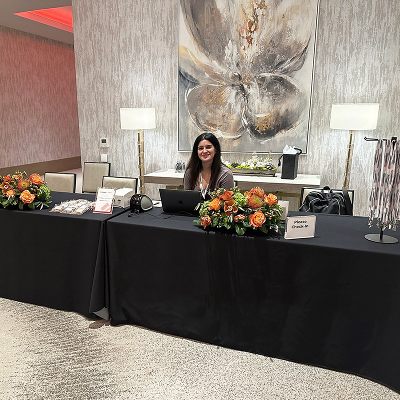 an event manager sits in front of a laptop at an event registration table ready to greet guests