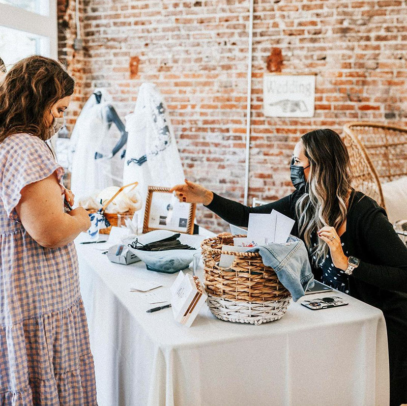 event planner at a registration table helping a guest with both people wearing face masks