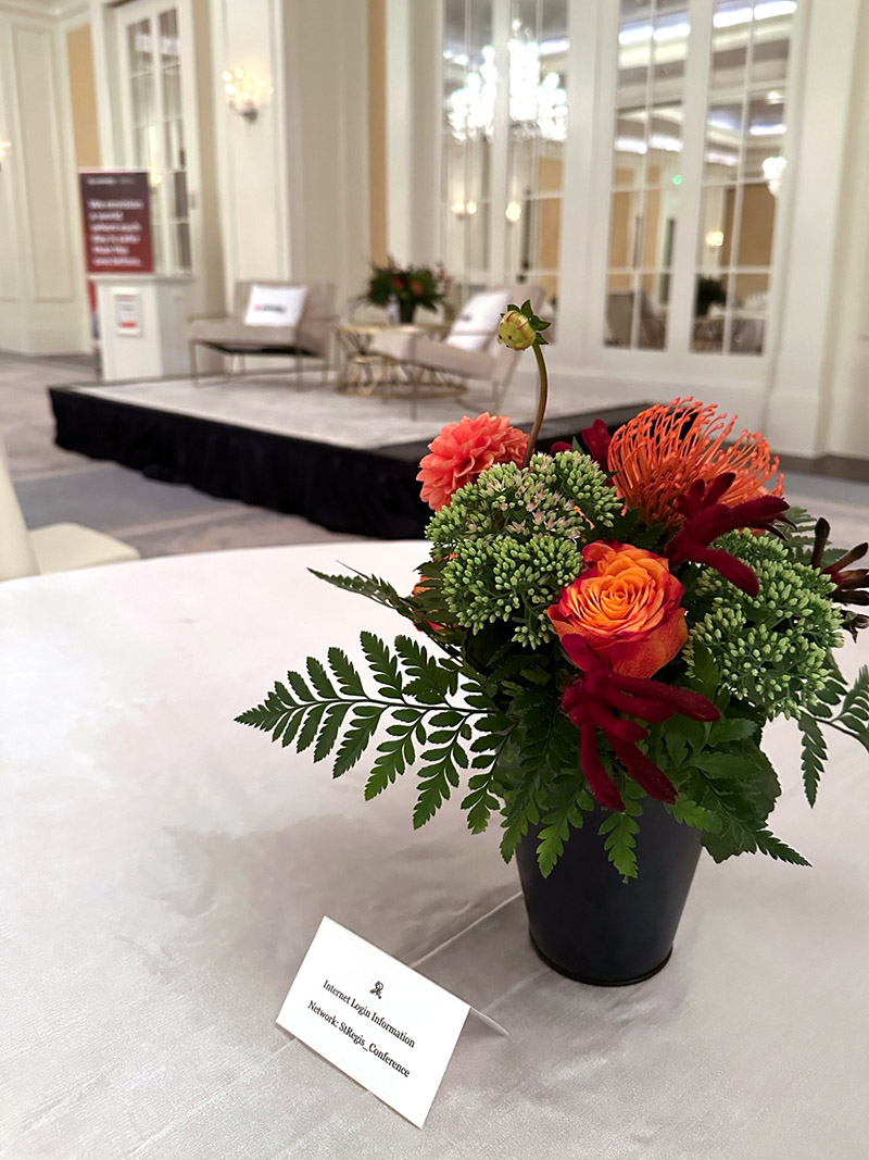 small bouquet of orange and white flowers on a round table with a stage in the background