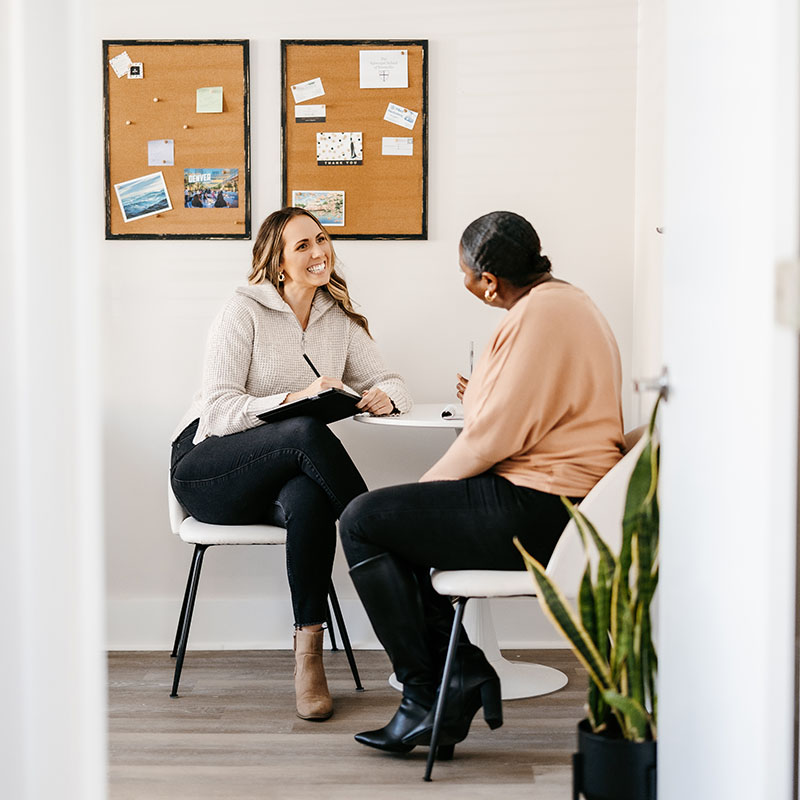 two women smiling and leaning in while having an amiable conversation