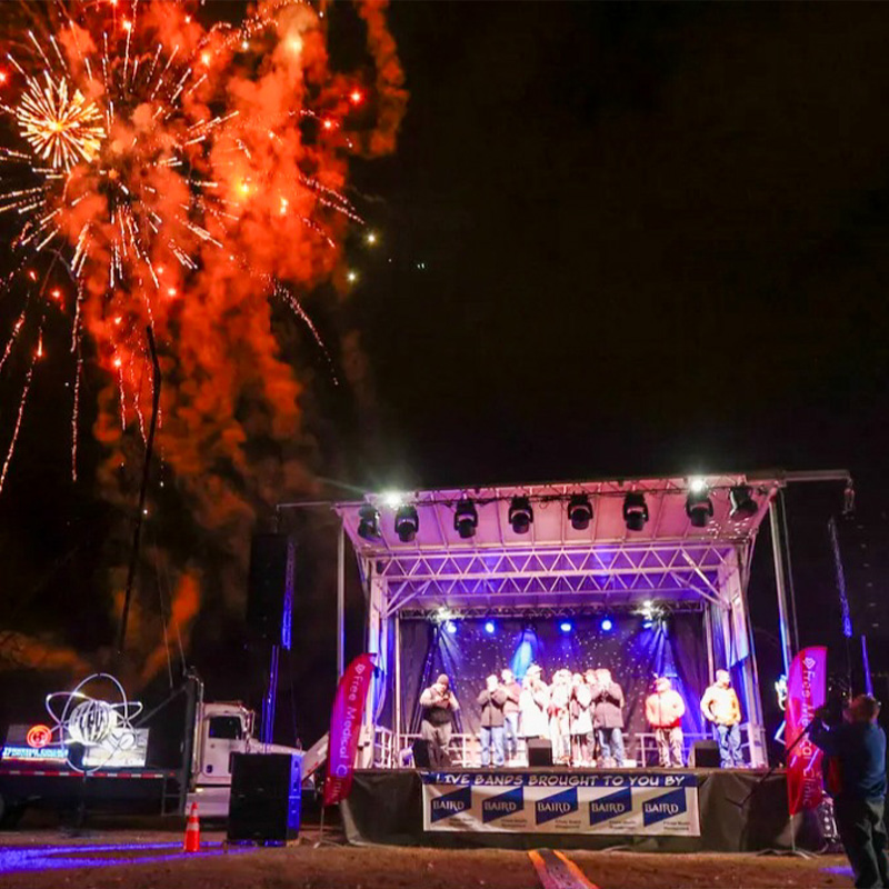 people standing on an outdoor stage with fireworks in the background