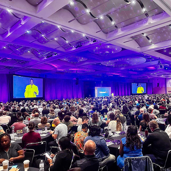 large hotel conference room with multiple screens and hundreds of people